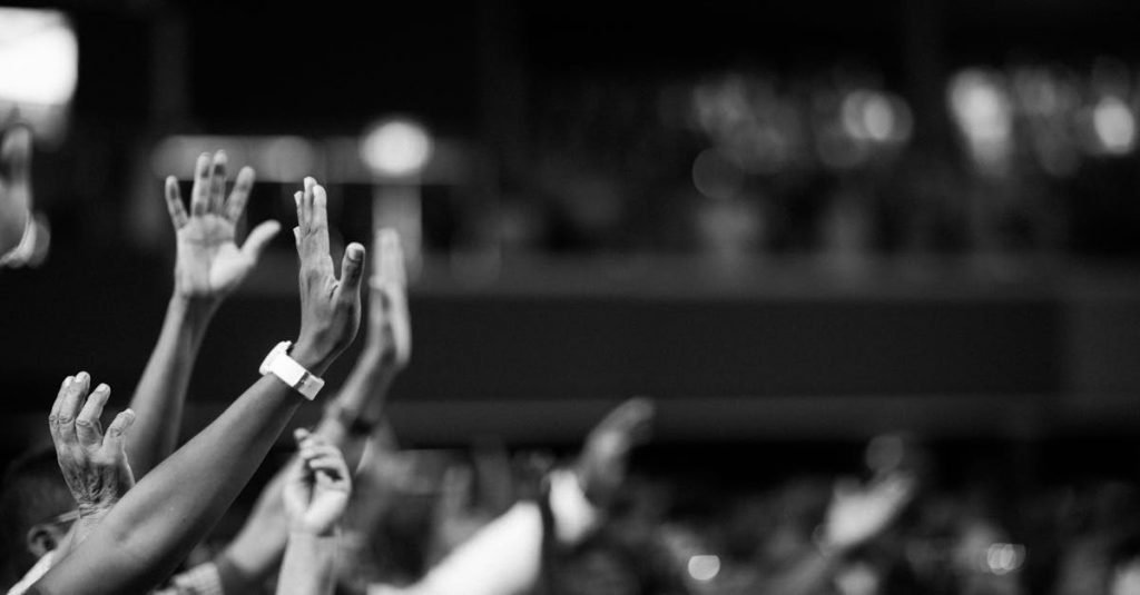 Black and white image of audience with hands raised, capturing concert energy.